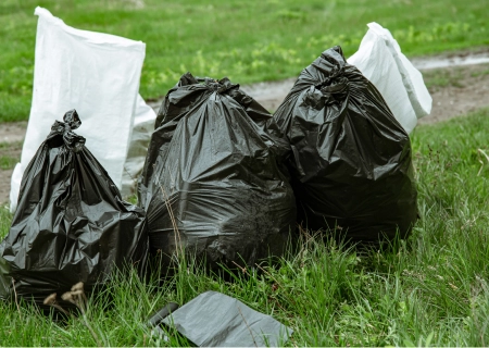Black garbage bags on grass near a dirt path, depicting waste management and environmental cleanliness.
