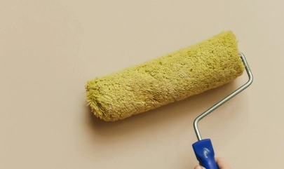 Painting Wall with Yellow Roller Brush on Beige Background