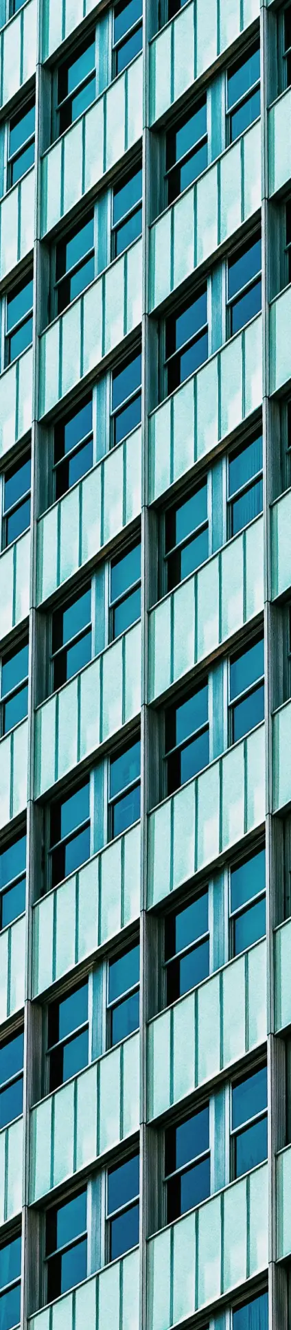 Modern high-rise building facade with uniform glass windows, teal panels, and vertical lines, creating a geometric pattern.
