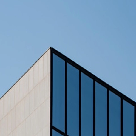 Modern glass building against clear blue sky, minimalistic architecture design with sleek lines and geometric shapes.