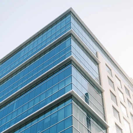 Modern glass office building with reflective windows under a clear sky, showcasing contemporary architectural design.