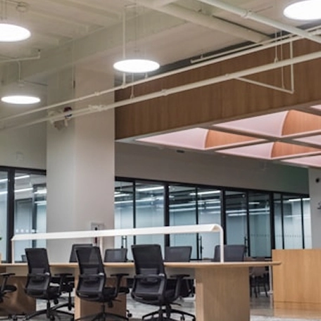 Modern office interior with open workspace, ergonomic chairs, wooden desks, and glass partitions under bright lighting.