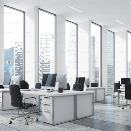 Modern office space with large windows, white desks, and black chairs, overlooking a cityscape.