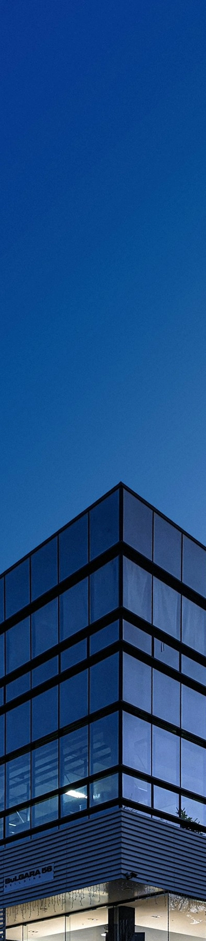 Modern glass office building at dusk against clear blue sky.