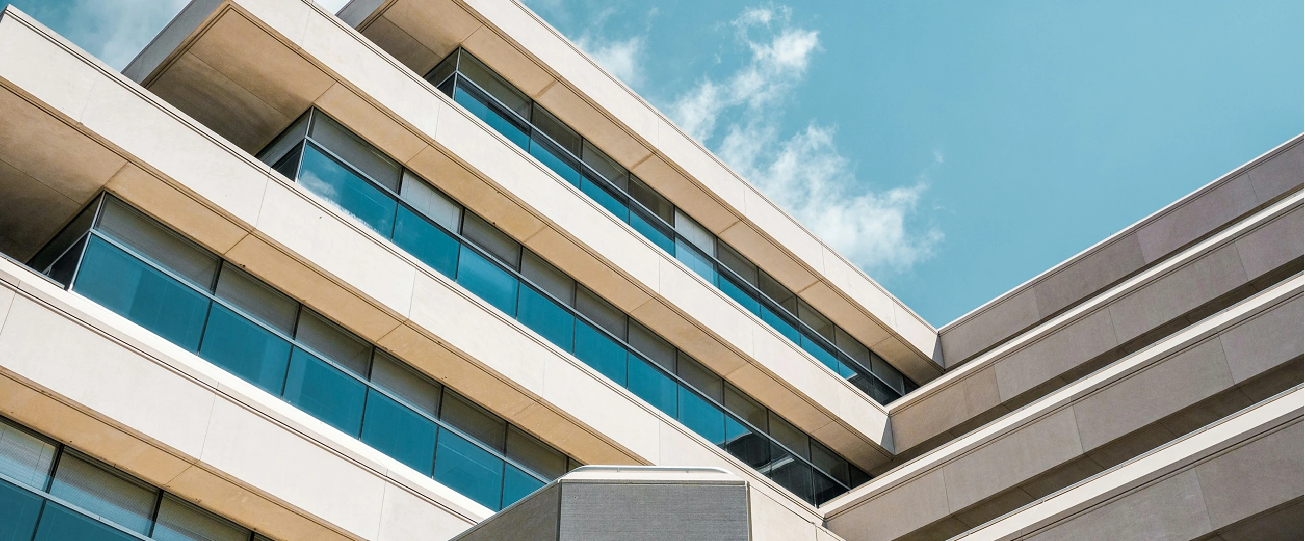 Modern office building facade with glass windows against a clear blue sky.