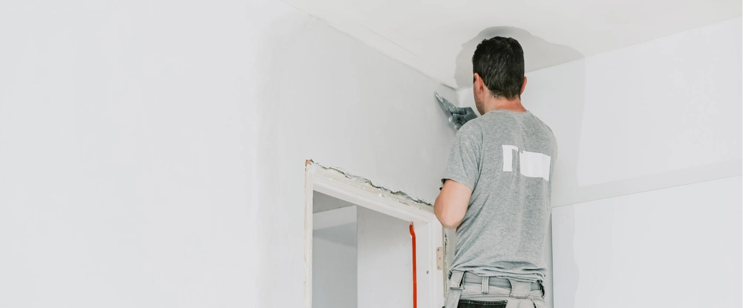 Man painting wall corner with roller, wearing casual gray t-shirt, engaged in home renovation project.