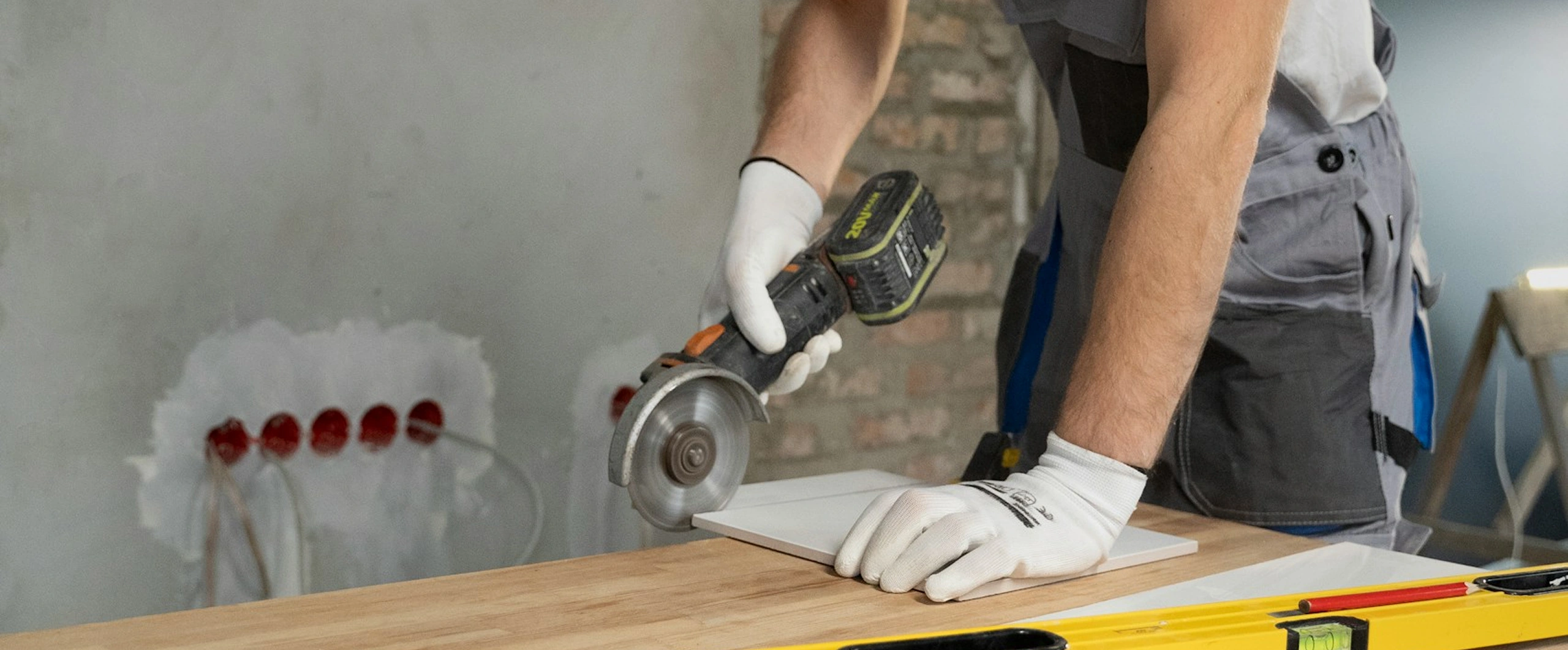 Worker using a circular saw to cut a tile on a wooden table with precision in construction setting.