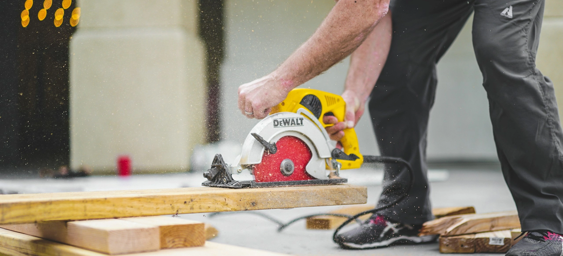 Man cutting wood with circular saw, using DeWalt tool, outdoors.