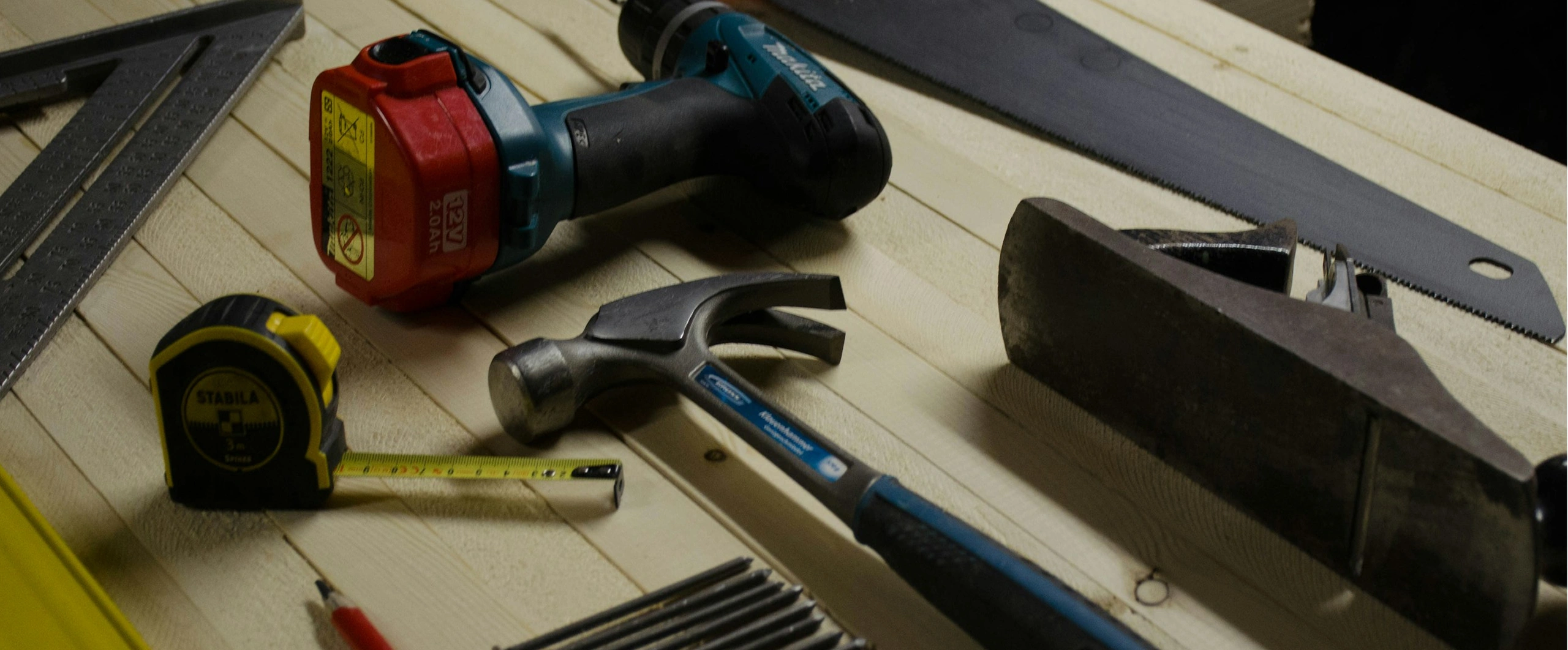 Woodworking tools including drill, hammer, and tape measure on a workbench.