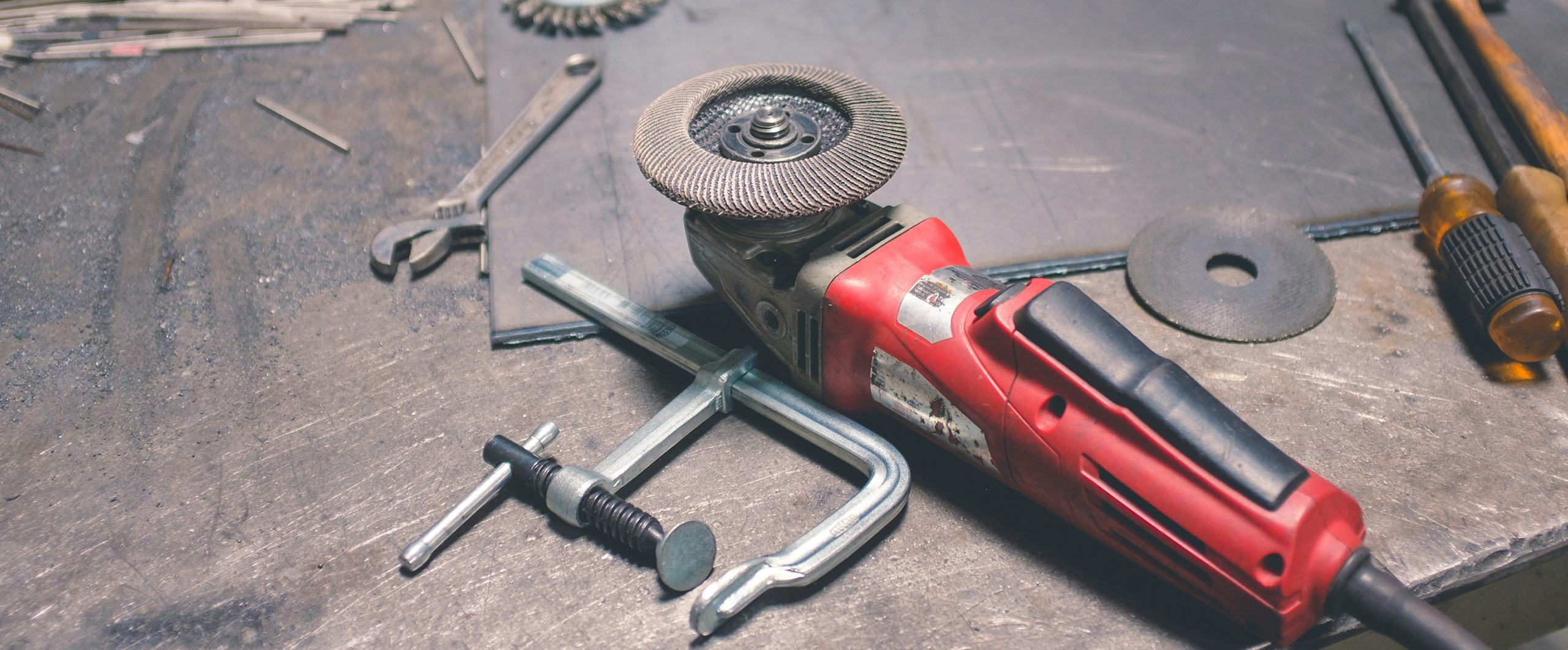 Professional handyman tools including an angle grinder, C-clamp, wrenches, and cutting disc on a metal workbench