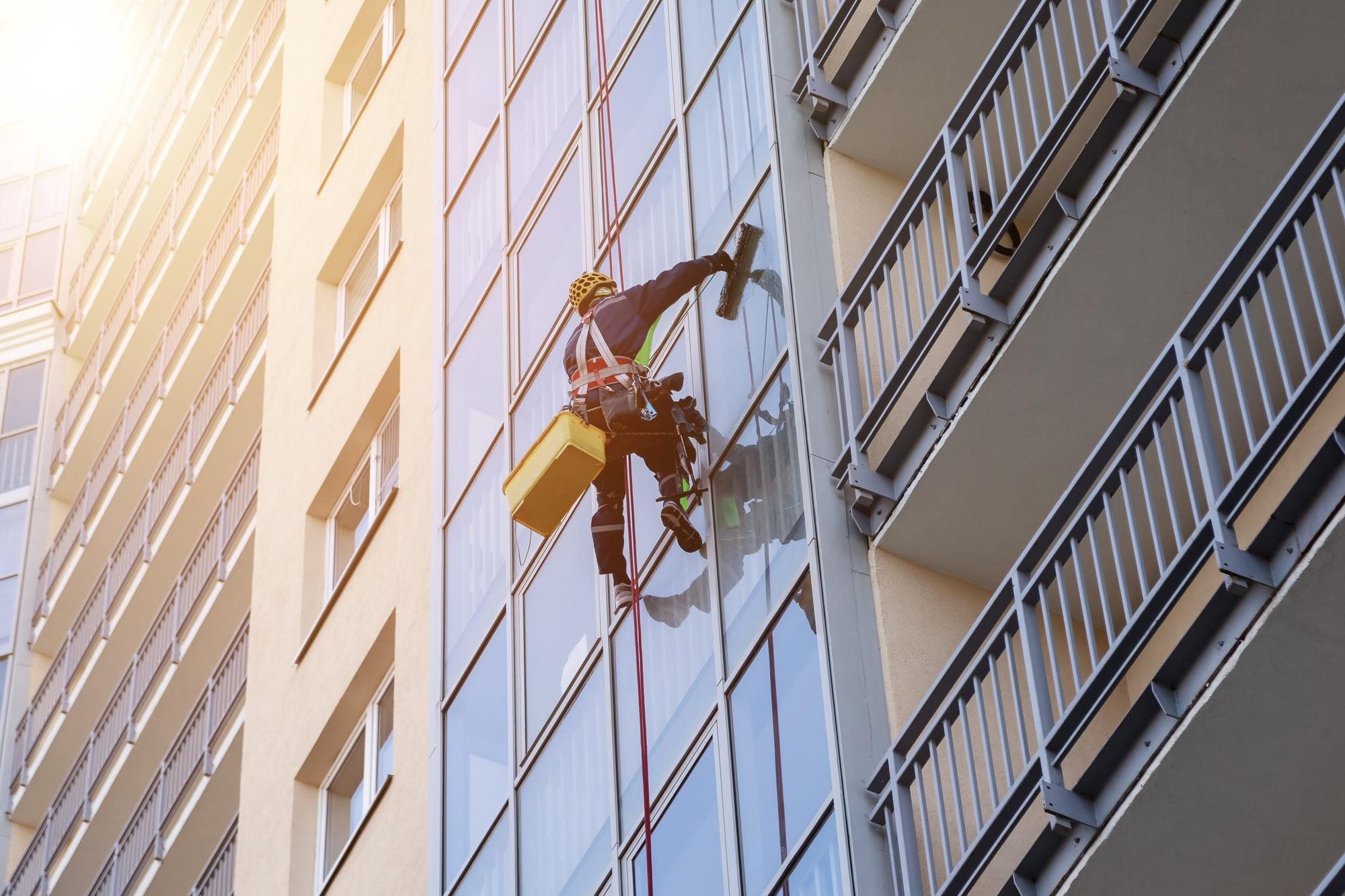Rope access technician in safety harness cleaning the glass facade of a high-rise apartment building