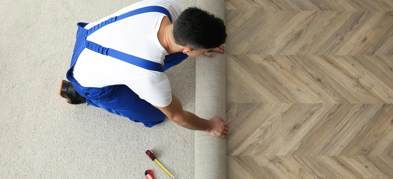 Technician rolling out carpet over a wooden floor.